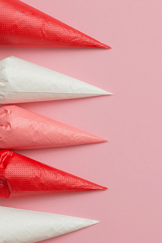 Piping bags filled with red, white, and pink icing on a light pink background.
