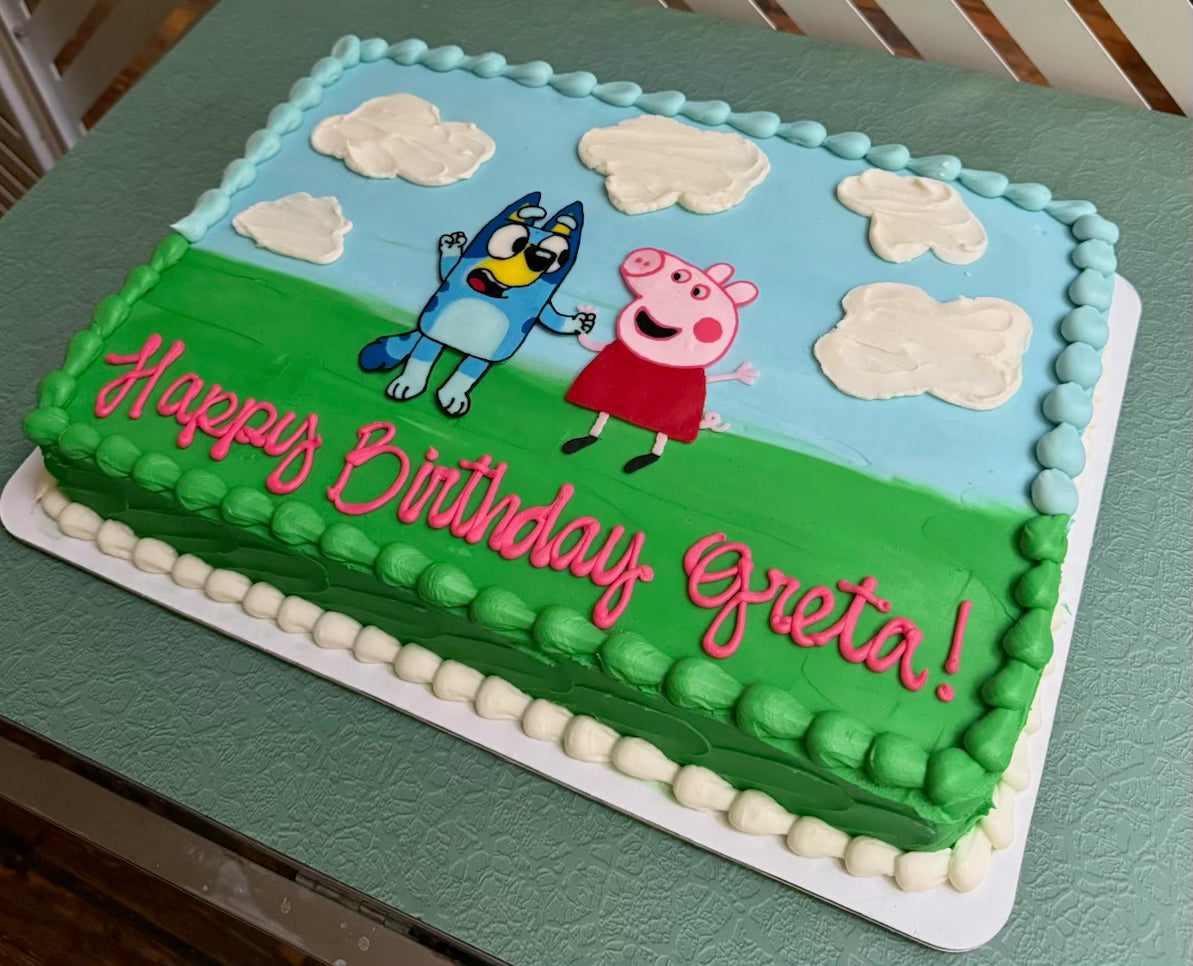 Birthday cake with cartoon characters and 'Happy Birthday Greta!' text on a green base.