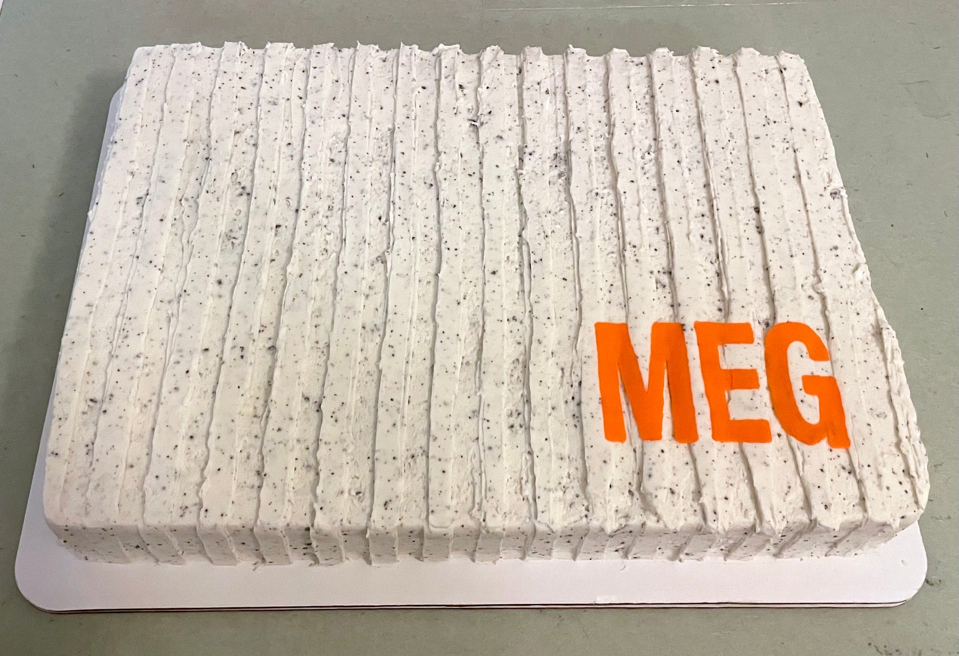 Rectangular cake with 'MEG' in orange letters on a gray background