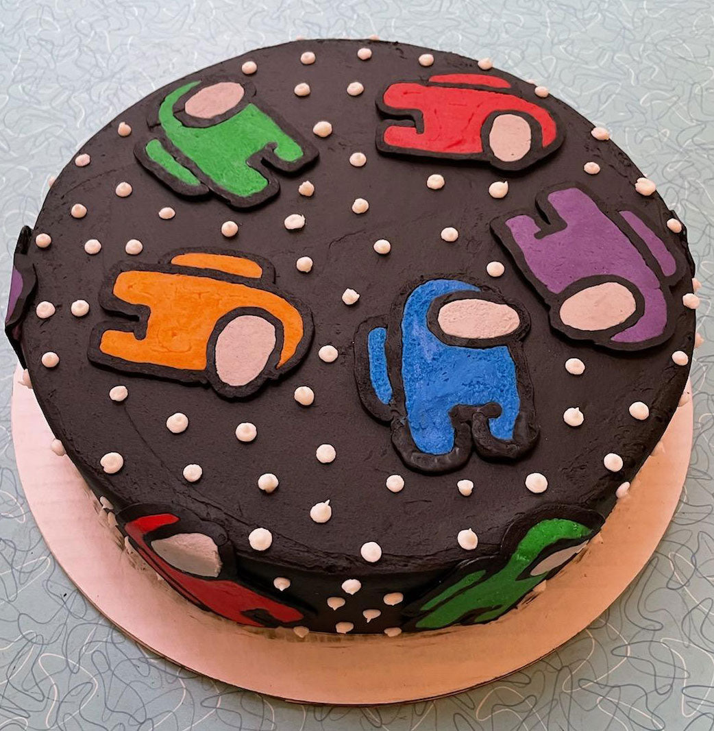 Round dark brown iced cake decorated with colorful 'Among Us' characters and white icing dots.