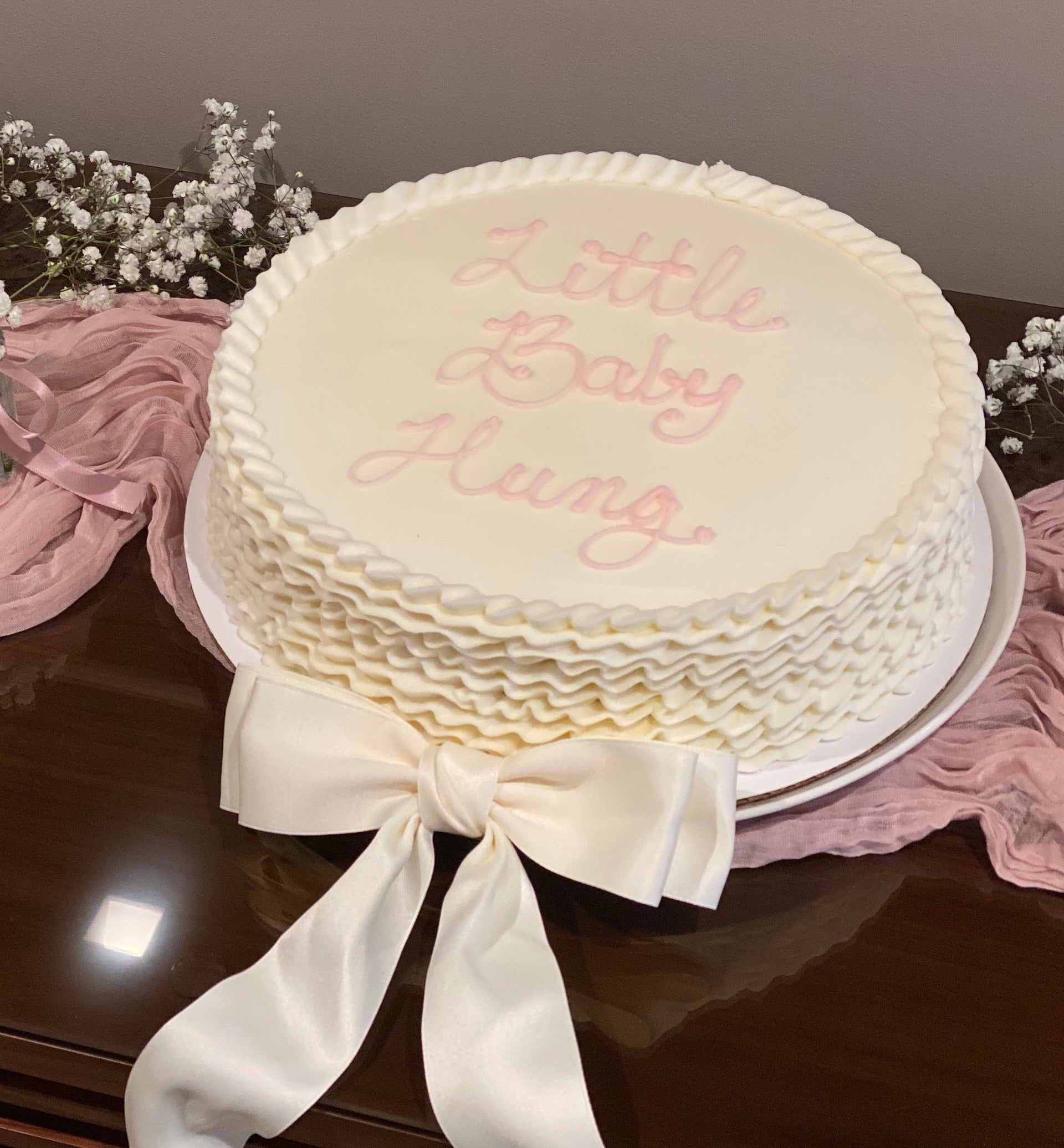White cake with 'A Little Baby Girl' text on a dark surface with flowers and ribbons.