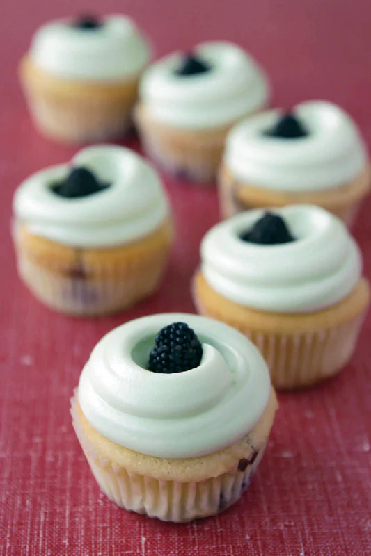 Cupcakes with white frosting and a blackberry on top on a red surface