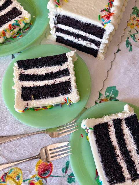 Slices of chocolate cake, frosted with white buttercream on green plates with colorful sprinkles.