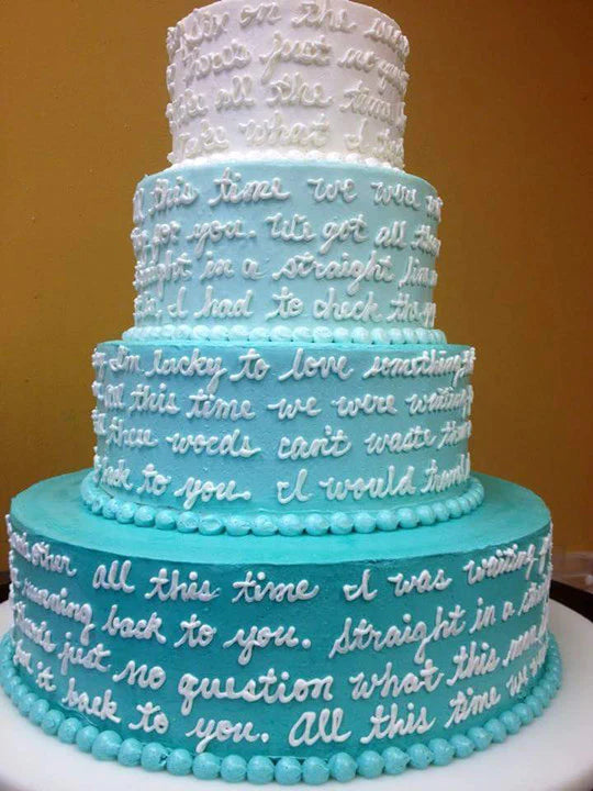 Multi-tiered wedding cake with blue ombre frosting and white icing text, featuring pearl-like border details on each tier.