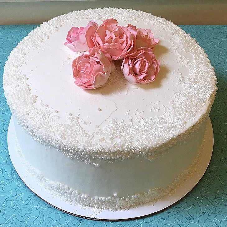 A white tiered cake decorated with white sprinkles and topped with five pink sugar flowers.