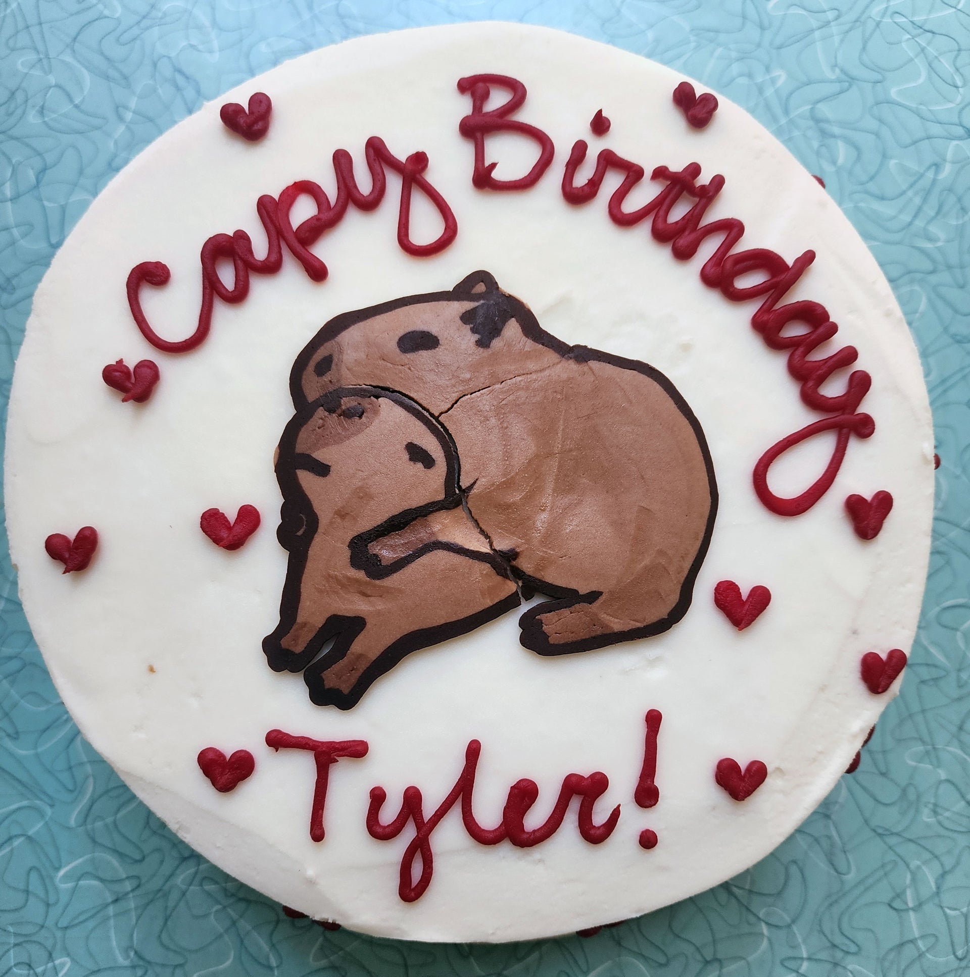 Birthday cake featuring two hugging capybaras and red heart decorations with the words "Capy Birthday Tyler!".
