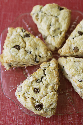 Five triangular chocolate chip scones on a clear plate with a red background.