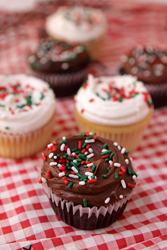 Cinco De Mayo cupcakes with white and chocolate frosting, topped with red, green, and white sprinkles, on a red and white checkered tablecloth.