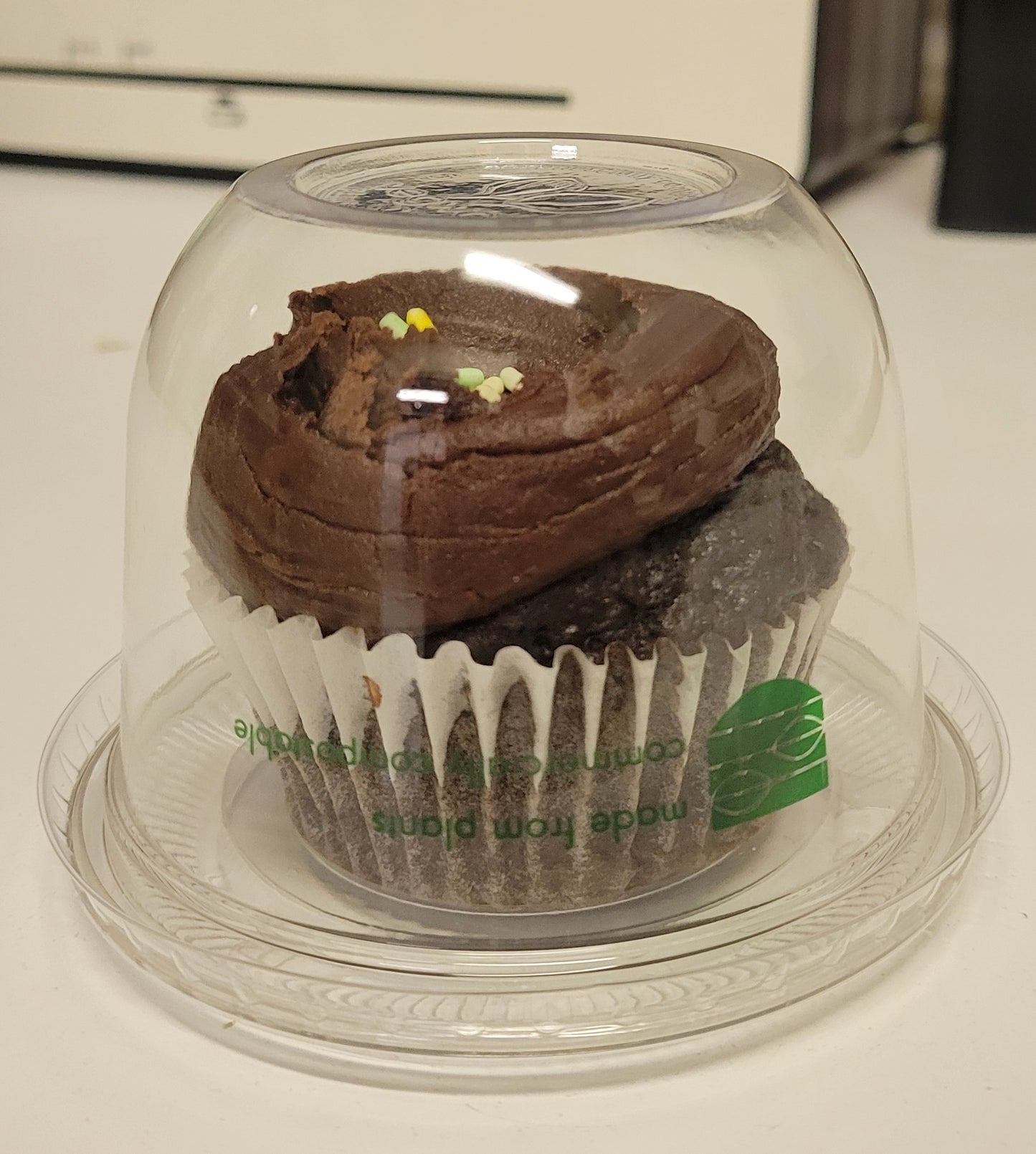 Chocolate cupcake under a clear dome on a white surface