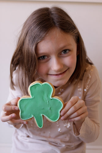A child holding a green shamrock-shaped sugar cookie.