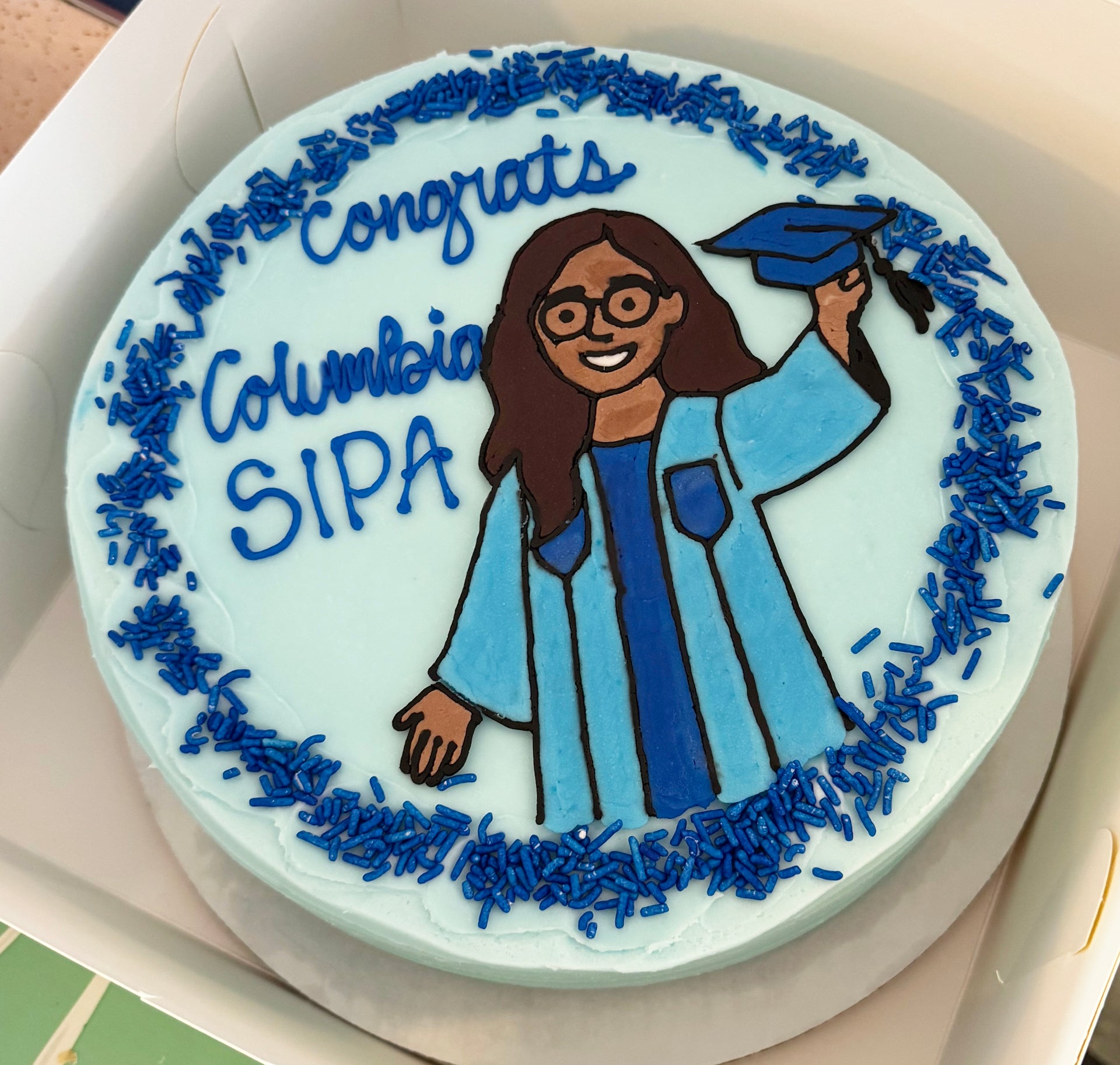 Graduation-themed cake with a graduate figure and 'Congrats Columbia SIPA' text on a white background.
