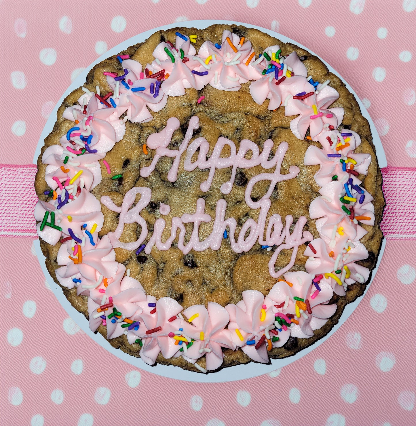 Cookie cake with pink frosting and 'Happy Birthday' text on a polka dot background