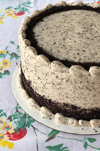 A chocolate cake with vanilla buttercream frosting, garnished with cookie crumbles, on a plate with a floral pattern in the background.