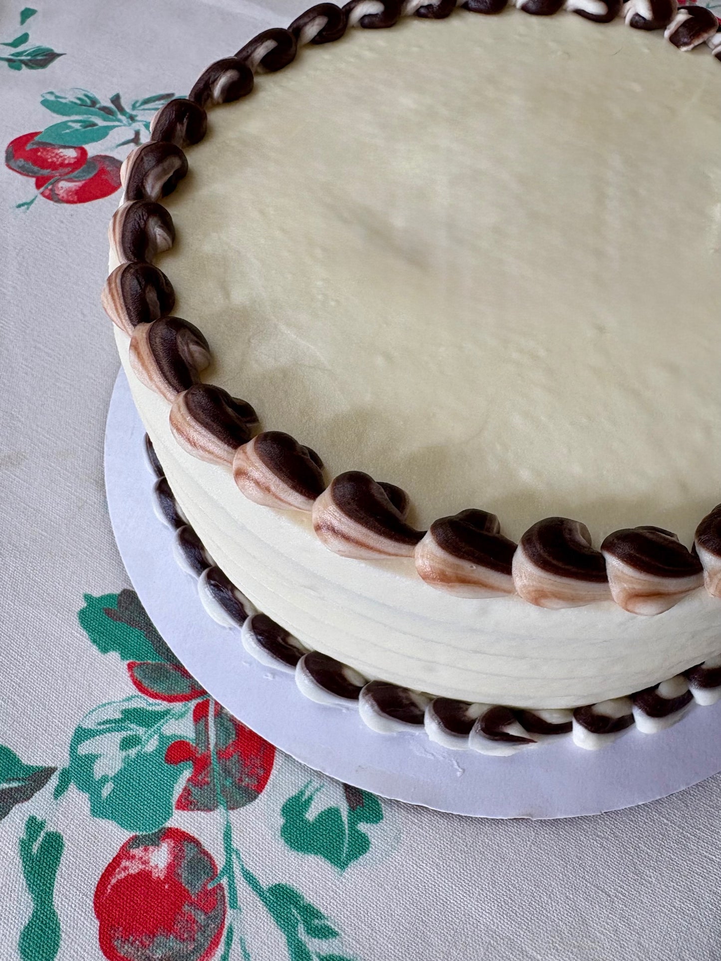 Round cake with white frosting and chocolate decorations on a floral tablecloth