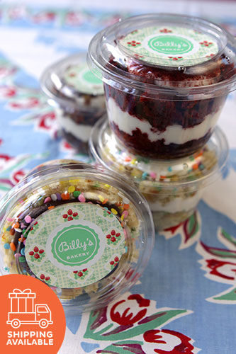 Clear plastic cups with various cupcakes inside, each cup has a different color and design lid, displayed on a table with a floral pattern.