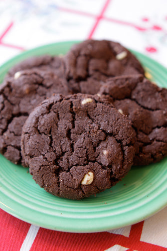 A plate of dark cocoa-flavored cookies filled with creamy white chocolate chips on a red and white checkered background.