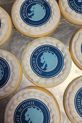 Round sugar cookies with white royal icing and edible images of the Dwight School logo featuring a blue lion silhouette and the text 'DWIGHT SCHOOL Igniting the spark of genius in every child'.
