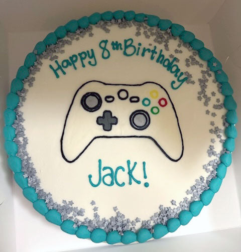 A round white birthday cake with blue piped icing around the border and "Happy 8th Birthday Jack" in the middle in blue icing.  There is a games controller drawing also in the centre of the cake.  