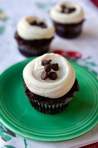 A chocolate cupcake with white frosting and chocolate chips on top, served on a green plate.