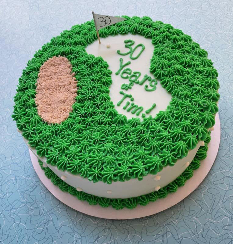 A round birthday cake decorated to resemble a golf course, with green frosting, a sandy bunker, a flag marking '30', and text '30 Years of Tim!'