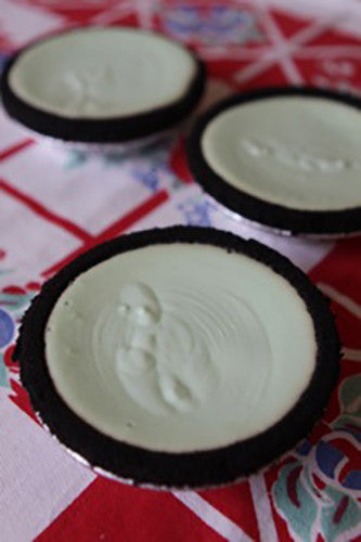 Sliced grasshopper pie with a green creamy filling and a chocolate crust on a red and white checkered surface.