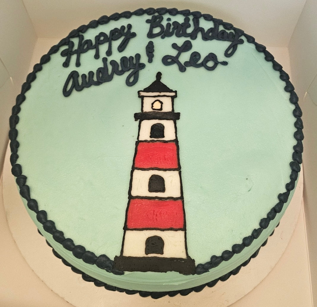 Birthday cake with a lighthouse design and 'Happy Birthday Audrey & Leo' text.
