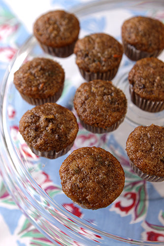 A clear glass container filled with carrot muffins, with a blue floral pattern in the background.