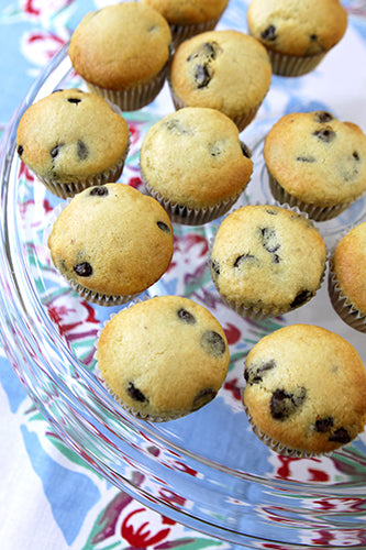 Close-up of golden-brown chocolate chip muffins on a clear glass cake stand.