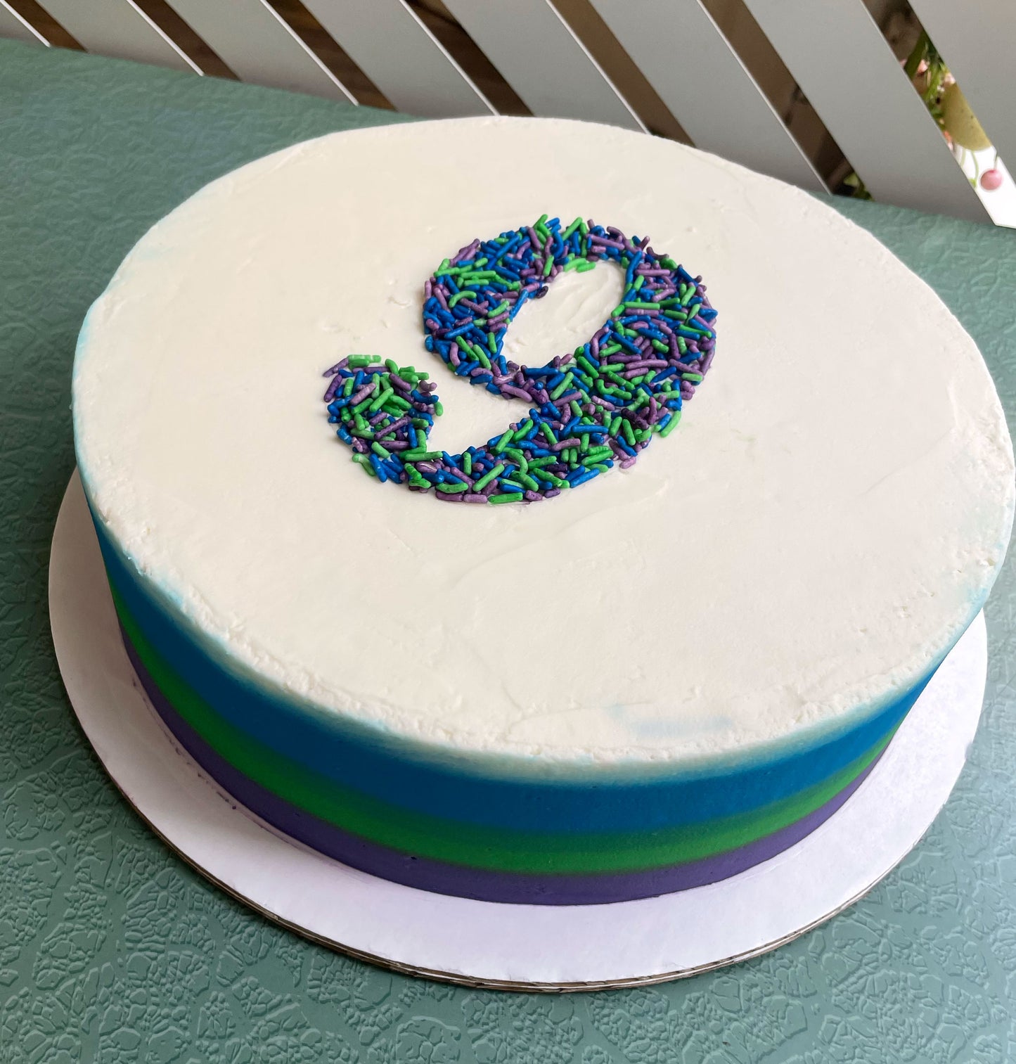 Round cake with number 9 made of colorful sprinkles on a green surface.