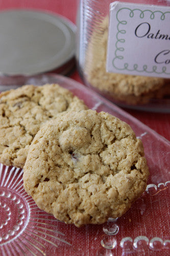 Delicious oatmeal raisin cookies on a decorative glass plate, with a jar of more cookies in the background. 