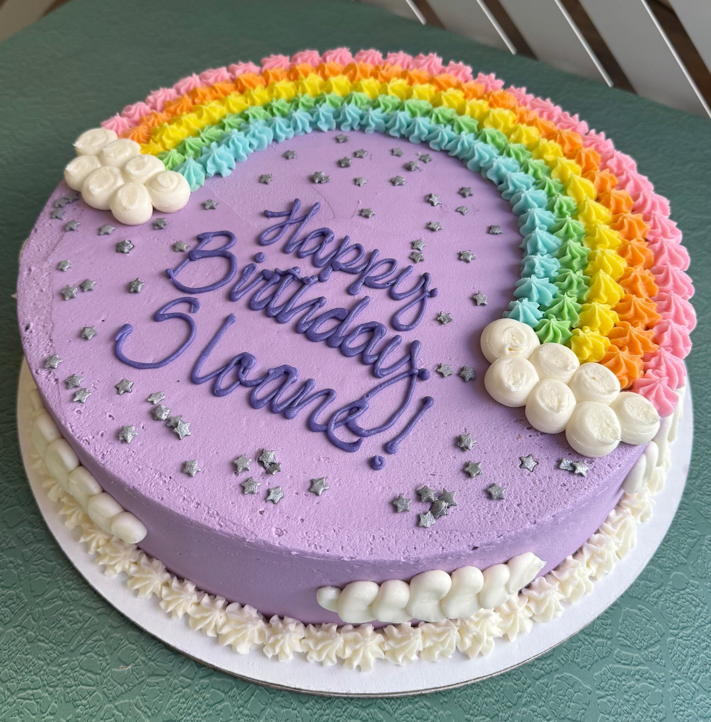 beautifully decorated birthday cake with a rainbow-shaped top, pastel colors, and the message 'Happy Birthday' in the center.