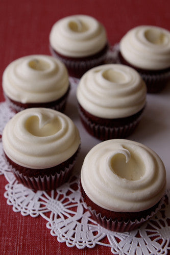 A group of red velvet cupcakes with cream cheese frosting presented on a plate with a lace doily.