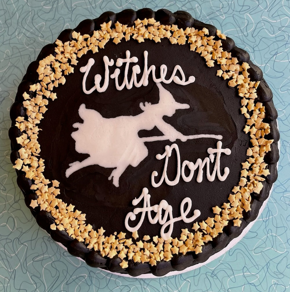 Cake with 'Witches Don't Age' text and witch silhouette on a decorative border.