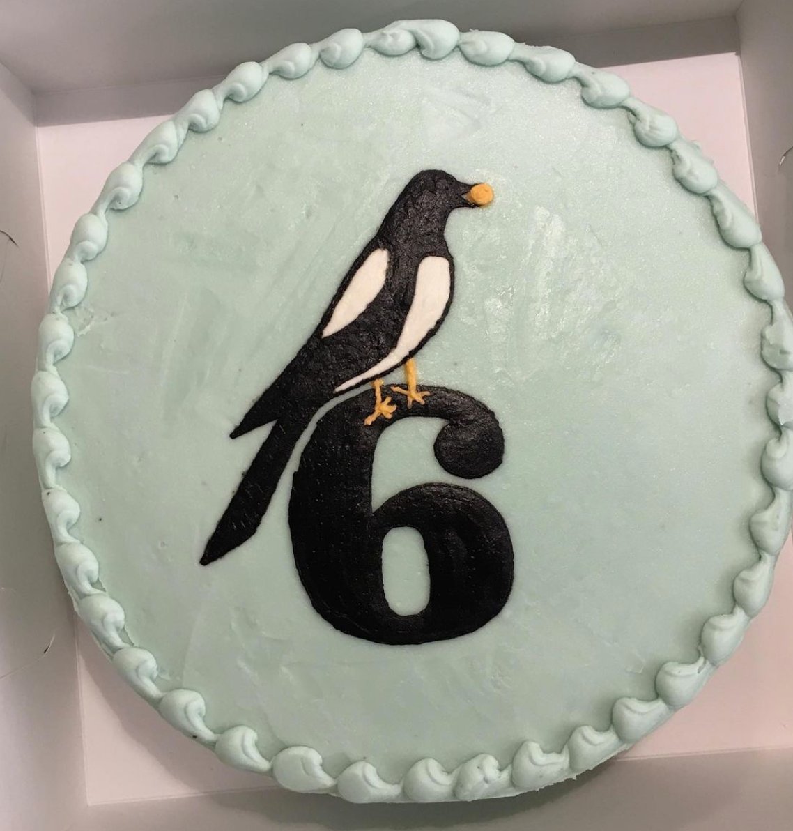 Cake with a bird and number 6 decoration on a light green background