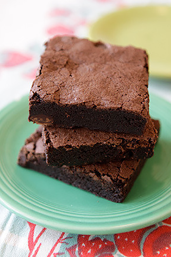 Stack of three chocolate brownies on a green plate, with more brownies visible in the background.