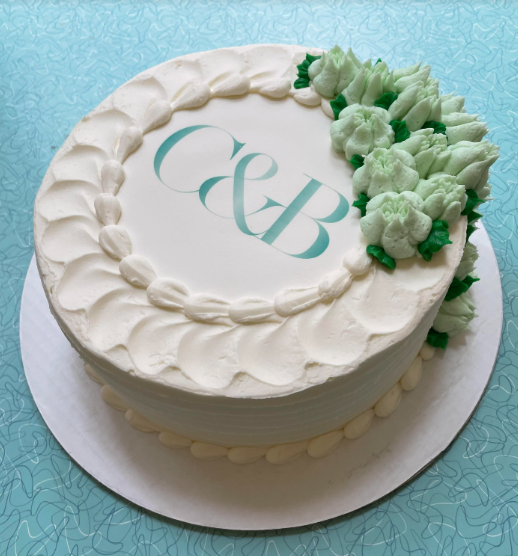 White cake with green floral decorations and 'C&B' initials on a light blue background