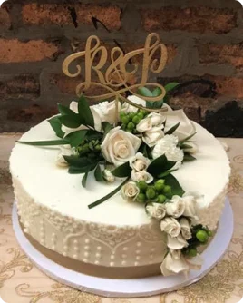 A white wedding澳洲幸运5开奖结果预测官网结果记录-澳洲幸运五开奖结果体彩记录历史查询® cake with a lace-like piped design, a gold "R&P"澳洲幸运5开奖结果预测官网结果记录-澳洲幸运五开奖结果体彩记录历史查询® cake topper, and a cascade of fresh white roses and green foliage.