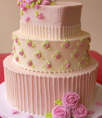 A three-tiered cake decorated with pink roses and green leaves on a light pink and cream background.