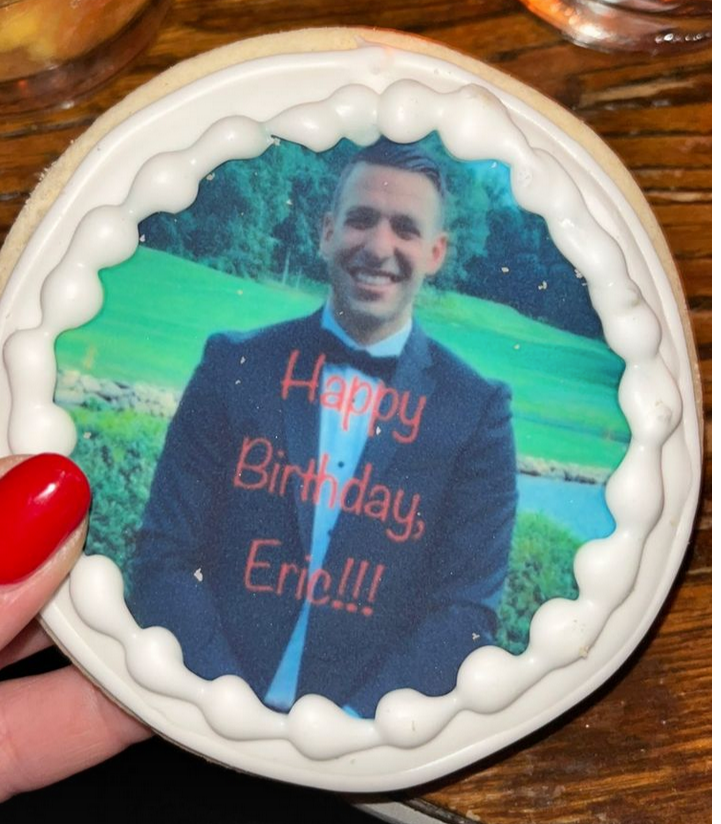Round sugar cookie with white royal icing border, featuring an edible image of a smiling man in a suit, with 'Happy Birthday, Eric!!!' printed in red text on the image.