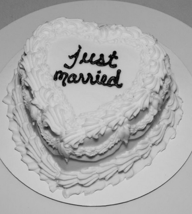 Heart-shaped white wedding cake with "Just married" written in black icing on top, on a white cake stand.